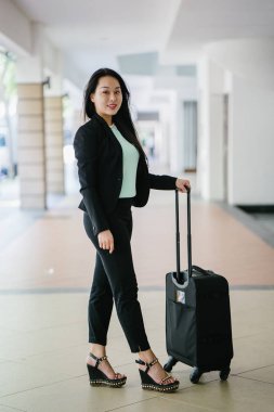 Genç bir Asyalı kadın bavulunu çekiyor. O çekici, zarif ve şık giyinmiş