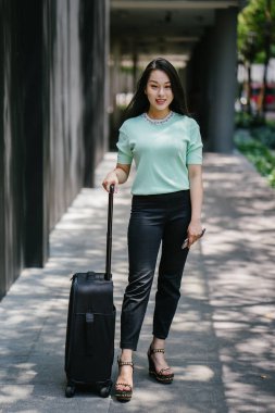 Genç bir Asyalı kadın bavulunu çekiyor. O çekici, zarif ve şık giyinmiş