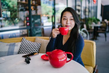 Bir açık havada açık havada oturan ve kırmızı bir çay seti çay sıcak bir fincan zevk genç, çekici, zarif ve güzel Asyalı kadın Portresi. 
