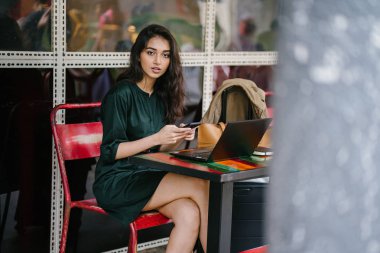 Genç Singpaorean Kızılderili kadın eğitim ya da bir kafede gün boyunca onu laptop çalışan bir mola alır gibi onun smartphone kontrol