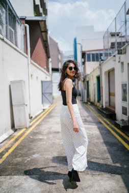 Genç, uzun boylu, ince ve zarif Hint Asyalı kadın rahat bir kıyafet içinde Asya bir sokakta bir sokakta aşağı gün boyunca yürür