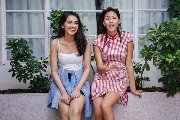 farklı etnik yapı birlikte dışarı asılı iki genç kadın arkadaşlar. Bir Çinli bir kadını bir cheongsam ve diğer bir Hint kadının modaya uygun bir kıyafet olduğunu