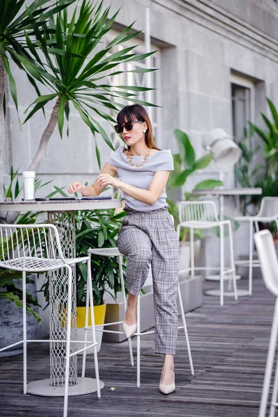 Açık havada şık bir yerde oturan bir emin, şık ve çekici orta yaşlı Çinli Asyalı kadın portresi. O bir pohpohlama gri kıyafeti giyiyor.