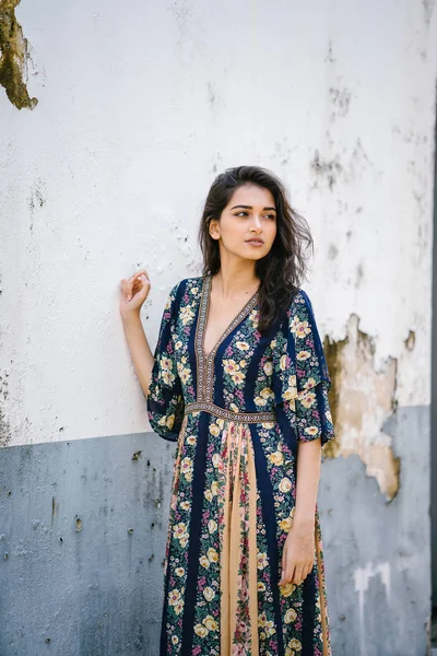 portrait of a tall, young, elegant and beautiful Indian Asian woman in flowing dress against a weathered wall on a street