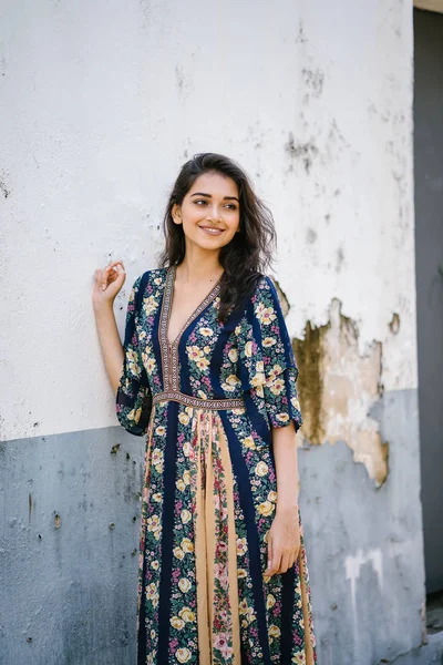 portrait of a tall, young, elegant and beautiful Indian Asian woman in flowing dress against a weathered wall on a street