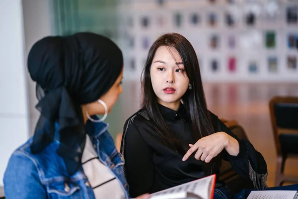 친구가 벤치에 합니다 하나는 무슬림 말레이인 여성이고 하나는 중국인 여성입니다 — 스톡 사진