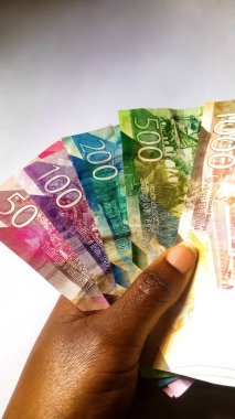 NAIROBI,KENYA-SEPTEMBER 18,2019: Different values of Kenya bank notes held by a colored hand against a white background. Image taken in Nairobi due to the new generation of currency in the country clipart