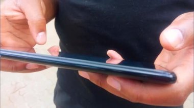 Genç bir adamın elleri, video klibi seçerken başparmak görüntüleriyle siyah bir tablet seçiyor. Afica 'lı adam. Çak bakalım. Kapatın. Akıllı telefon hayatı. Sıradan giyinmiş. Elektronik cihaz. Çeşitlilik.
