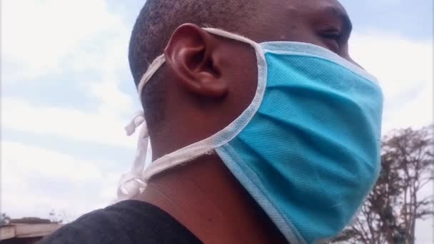 青い外科用マスクをした男が頭を回して辺りを見回していた アフリカ民族 ハンサムだな 屋外だ Coronavirus Covid 2019 Ncv 閉めろ サイドビュー — ストック動画