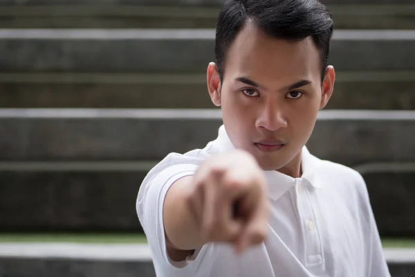 pointing man portrait; serious man pointing finger gesture; asian man points at you with serious mood emotion; young adult south east asian man model with tan skin and short hair