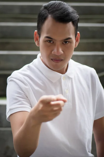 pointing man portrait; serious man pointing finger gesture; asian man points at you with serious mood emotion; young adult south east asian man model with tan skin and short hair