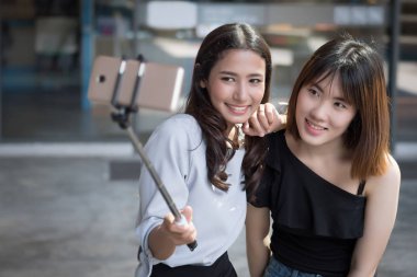 mutlu bir kadın en iyi arkadaşı selfie fotoğraf birlikte alarak; hobi, eğlence, rahat selfie fotoğraf kentsel ortamda almaya selfie stick kullanarak onu kanka ile Asyalı kız gülümseyerek; Asya 20'li yaşlarda kadın modeli
