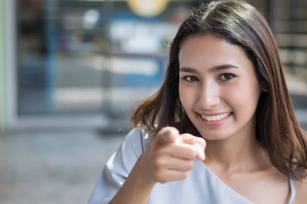 happy girl pointing at you; portrait of cheerful smiling woman points hand and finger to camera; concept of inviting, invitation, picking, selecting, selection pointing; asian woman young adult model