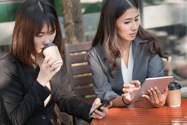 casual business meeting in coffee shop; portrait of business woman, business people, business team working in team with mobile devices, tablet, smart pone or smartphone; asian 20s adult woman model