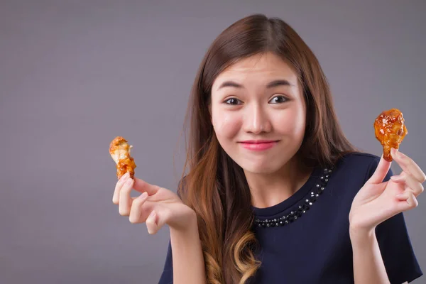 asian woman eating fried chicken; portrait of beautiful woman, happy girl eating spicy, crispy fried chicken studio isolated; food, snack, eating, dining concept; asian chinese young adult woman model