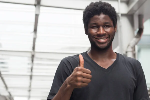 successful african man pointing thumb up; portrait of cheerful smiling african man or black man pointing up approving, yes, ok, good, thumb up gesture; young adult african man model