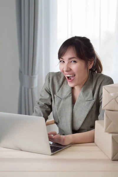 excited asian woman working with her laptop computer and courier parcel box; portrait of excited, happy woman business owner with business success or profit concept; adult asian chinese woman model