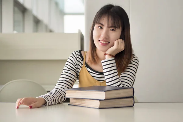 happy smiling woman college student gets back to school with a stack of books; portrait of positive, confident, relaxed woman university student studying in library; asian young adult woman model