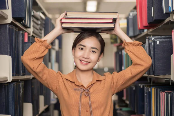 smart woman college student searching books; portrait of happy smiling woman university student studying, reading, finding book or textbook in library; asian young adult woman model