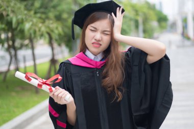 mutsuz, kadın Üniversitesi öğrenci mezun vurguladı; mezuniyet derecesi ile baş ağrısı stres, zor eğitim kavramı ile diploma veya üniversite kadın öğrenci portresi; Asyalı Genç Yetişkin kadın modeli