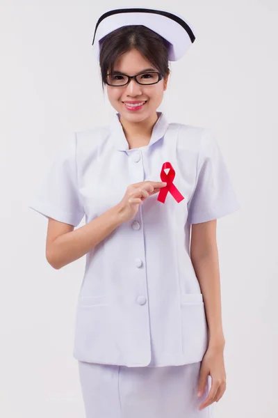 woman nurse hand holding red ribbon bow, hiv or aids awareness symbol presented by woman in studio shot. medical, charity, nurse fund raising concept for red ribbon hiv aids day awareness