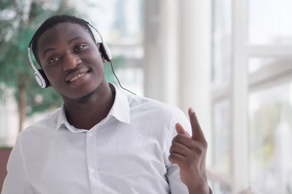 Modern African man listening to music headsets and pointing up; portrait of happy smiling Black African man enjoying digital mobile music player device; African man young adult model