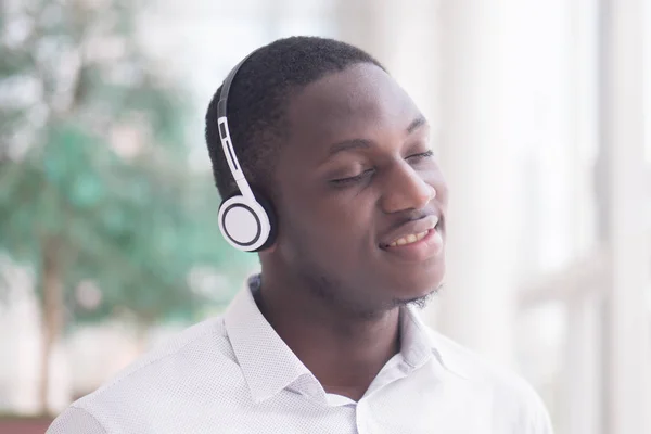 Modern African man listening to music headsets; portrait of happy smiling Black African man enjoying digital mobile music player device; African man young adult model