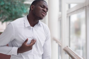 Asit reflüsü veya GERD 'den muzdarip Afrikalı bir adam; hazımsızlık, asit reflüsü veya gerd semptomları olan hasta stresli siyahi bir adam; erkek sağlığı, vücut bakımı, hastalık, ağrı konsepti; yetişkin Afrikalı erkek modeli;