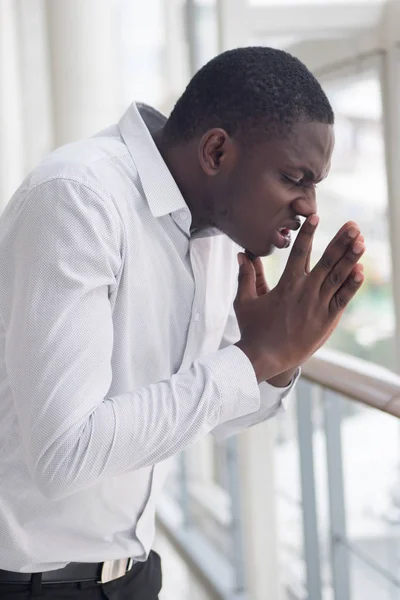 Sick African man sneezing due to allergy; Portrait of allergic African man sneezes due to cold, flu, allergy, polluted air, fine dust; air pollution, lung disease concept; African man model