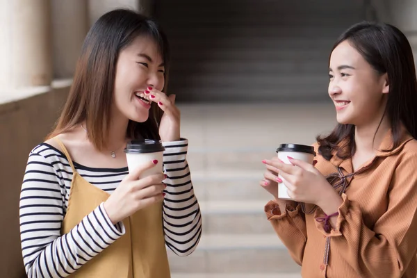 asian woman friend talking about gossip; portrait of laughing, smiling woman drinking coffee while gossiping, concept of friendship, social trend, news update; young adult asian woman model