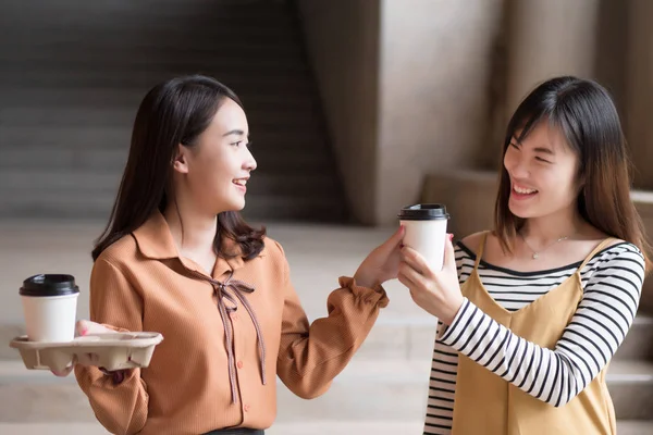 asian woman friend sharing coffee; portrait of two friendly woman giving coffee, concept of friendship, sharing; young adult asian woman model