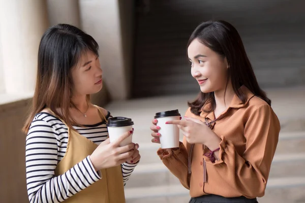 asian woman friend talking about gossip; portrait of two friendly woman drinking coffee while gossiping, concept of friendship, social trend, casual news update; young adult asian woman model