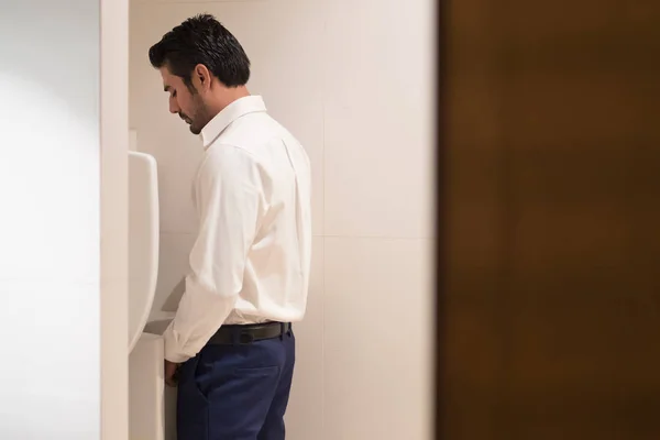 A woman wearing white jeans is pissing in the public toilet