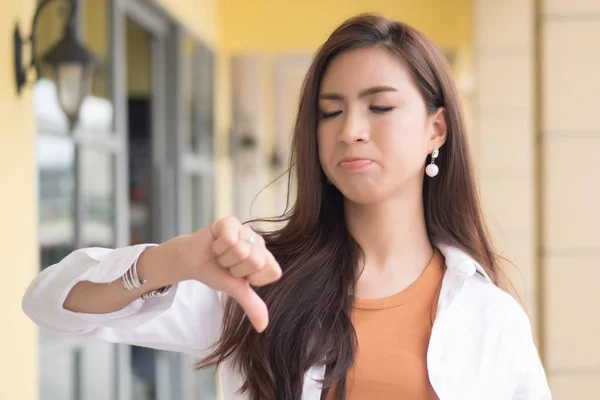 angry woman pointing thumb down; portrait of angry upset frustrated negative woman pointing up disapproval, no, bad, rejecting thumb down gesture; asian chinese woman young adult model