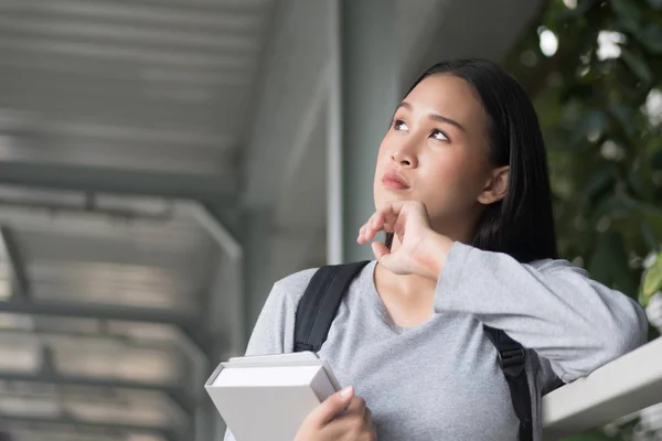 portrait of thoughtful asian woman college student thinking and looking up at possible education future, city campus environment