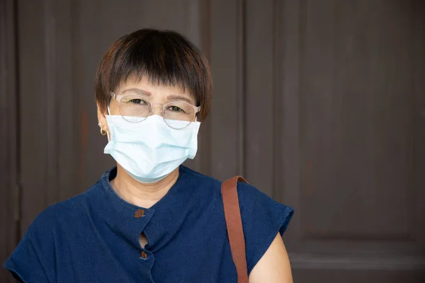 middle aged woman wearing face mask, observing new normal social distancing measure to flatten the curve and prevent virus infection by taking physical distance, covering her face with facemask