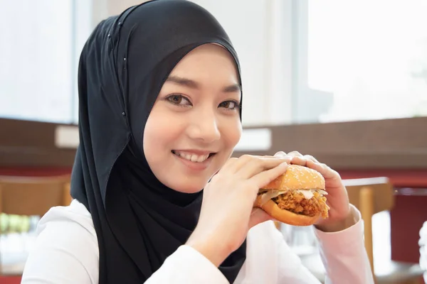 空腹のイスラム教徒の女性を探して ハラールフライドチキンバーガーを食べる おいしいハラール食品の概念 ファーストフード 健康管理 習慣を食べる クリスピーおいしいフライドチキンバーガー アジアのイスラム教徒の女性モデル — ストック写真