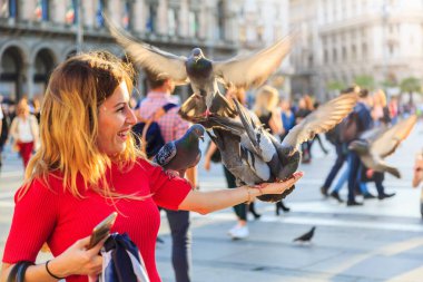 Milan, İtalya - 17 Nisan 2018 - güvercin bazı tahıl ile piazza Duomo di Milano önünde, onun yandan besleme ise belirsiz Avrupa kadın gülümsüyor.