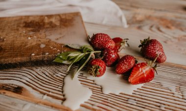 Masanın üzerine taze sulu kırmızı çilekler ve kaliteli kalaslar serpiştirdim. Nane yaprağı. Damlalar ve dökülen sütler. Sebze kesme tahtası. Yüksek kalite fotoğraf