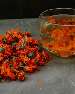 Şeffaf büyük bir fincanda çiçek çayı. Şifalı bitkisel kurutulmuş bitkiler kadife çiçeği, turuncu takvim. Tarafsız beyaz ve gri arkaplan.