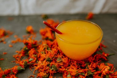 Küçük bir fincan ağzına kadar sarı sıvı bal ile doldurulur. Şifalı bitkisel kurutulmuş bitkiler kadife çiçeği, turuncu takvim. Tarafsız beyaz ve gri arkaplan.
