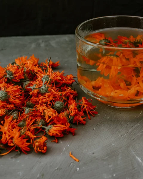 Şeffaf büyük bir fincanda çiçek çayı. Şifalı bitkisel kurutulmuş bitkiler kadife çiçeği, turuncu takvim. Tarafsız beyaz ve gri arkaplan.