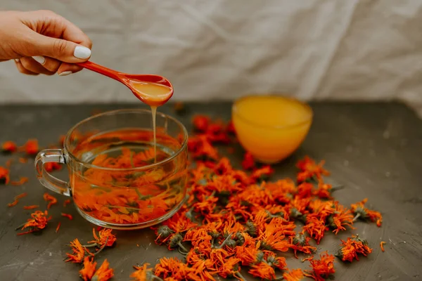 Bir kadının eli, kaşıktan fincana bal döker. Büyük şeffaf bir fincanda çiçek çayı. Küçük bir bardak, tepesine sarı sıvı bal doldurulur..