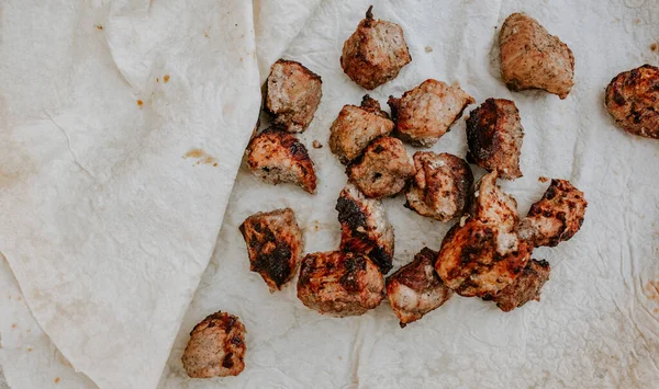 Pork veal cow meat cut into square pieces and fried over a fire lies on a thin white pita bread.