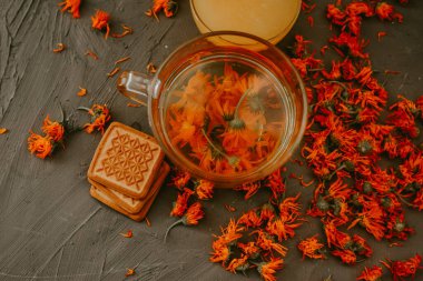 Calendula çiçekli ve bisküvili çay. Şeffaf cam bardak ve çay tabağı