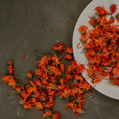 Gri bir tabakta kurumuş çiçekler, turuncu bir takvim..