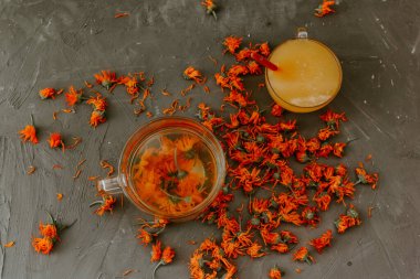 Büyük şeffaf bir kupada çiçek çayı. Küçük bir bardak ağzına kadar sarı sıvı bal ve turuncu takvimle doldurulur..