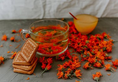 Calendula çiçekli ve bisküvili çay. Şeffaf cam bardak ve çay tabağı