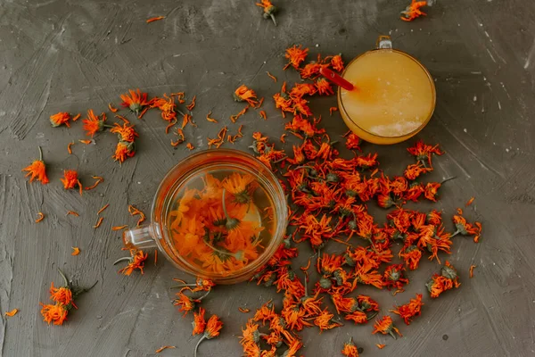 Büyük şeffaf bir kupada çiçek çayı. Küçük bir bardak ağzına kadar sarı sıvı bal ve turuncu takvimle doldurulur..