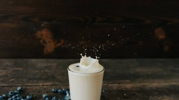 Jagody są wrzucane do przezroczystego szkła, tworząc plamy mleka. — Zdjęcie stockowe